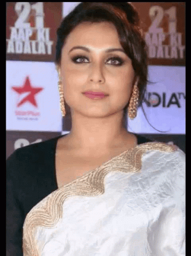 A Woman Is Wearing A White And Gold Saree And Earrings GIF