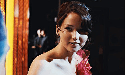 A Woman Is Wearing A White Dress With A Pink Flower On The Shoulder GIF