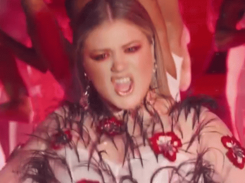 A Woman Is Wearing A White Dress With Feathers And Flowers On It And Making A Funny Face . GIF