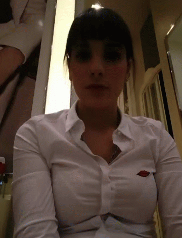 A Woman Is Wearing A White Shirt With A Logo On The Breast GIF