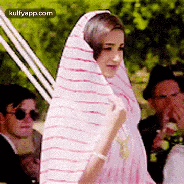 A Woman Is Wrapped In A Pink And White Striped Shawl . GIF