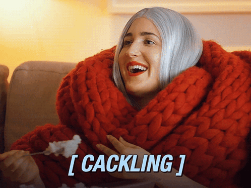 A Woman Is Wrapped In A Red Blanket And Eating Popcorn With The Caption [ Cackling ] GIF