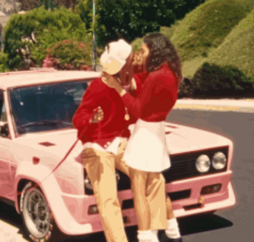 A Woman Kissing A Man On The Cheek In Front Of A Pink Car GIF