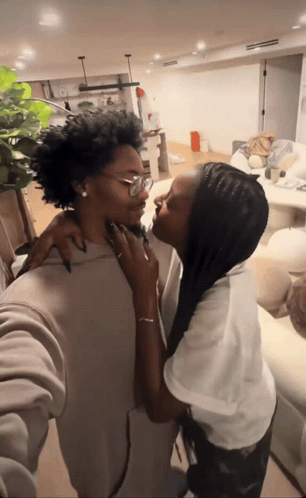 A Woman Kissing Another Woman 'S Neck In A Living Room GIF