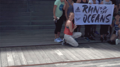 A Woman Kneeling Down Holding A Banner That Says Run For The Oceans GIF