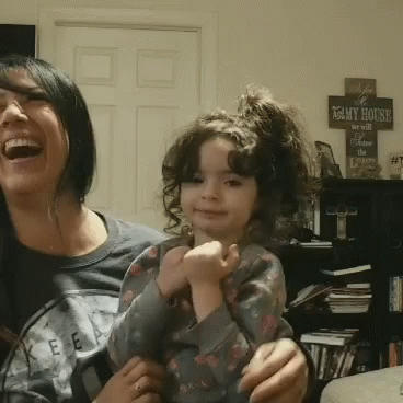 A Woman Laughs While Holding A Little Girl In Front Of A Sign That Reads " My House " GIF