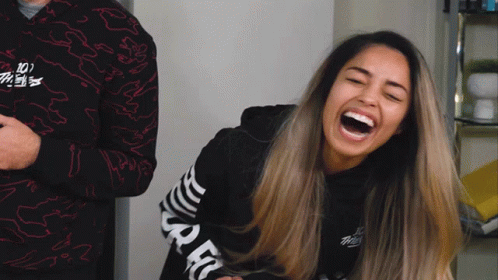 A Woman Laughs While Wearing A Black Shirt With The Word Spec On The Sleeves GIF
