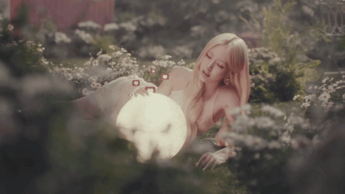 A Woman Laying In A Field Of Flowers Holding A Light GIF