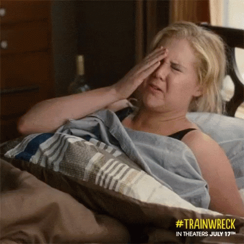 A Woman Laying In Bed With Her Hand On Her Forehead GIF