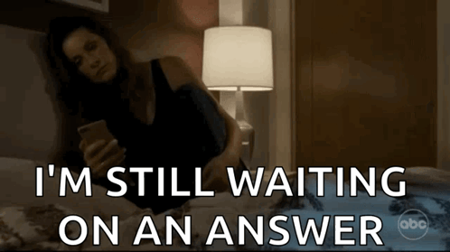 A Woman Laying On A Bed Looking At Her Phone With The Words I 'M Still Waiting On An Answer GIF