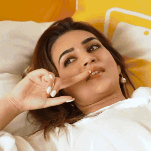 A Woman Laying On A Bed Making A Face With Her Finger In Her Mouth GIF