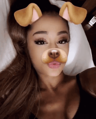 A Woman Laying On A Bed With A Dog Face Filter On Her Face GIF