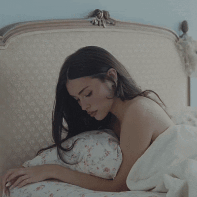 A Woman Laying On A Bed With A White Blanket GIF