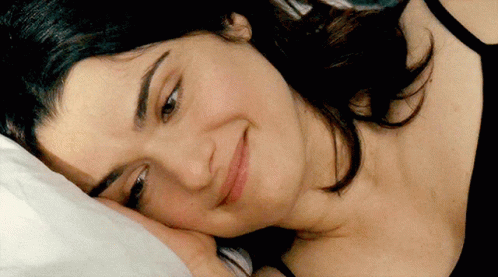 A Woman Laying On A Bed With Her Head On A Pillow And Smiling GIF