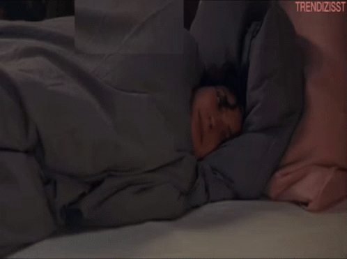 A Woman Laying On A Bed With The Words Trendizisst On The Bottom Right GIF