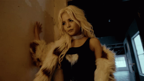 A Woman Leaning Against A Wall Wearing A Fur Coat And A Choker GIF