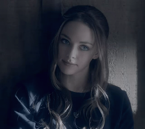 A Woman Leaning Against A Wall With A Serious Look On Her Face GIF