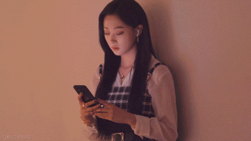 a woman leans against a wall looking at her phone