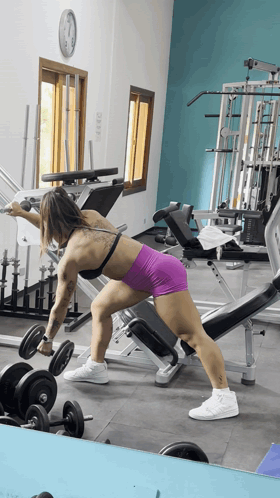 A Woman Lifting A Dumbbell In A Gym With A Clock On The Wall GIF