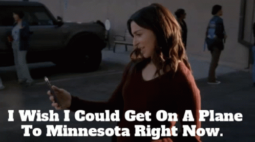 A Woman Looking At Her Phone With The Words " I Wish I Could Get On A Plane To Minnesota Right Now " Above Her GIF