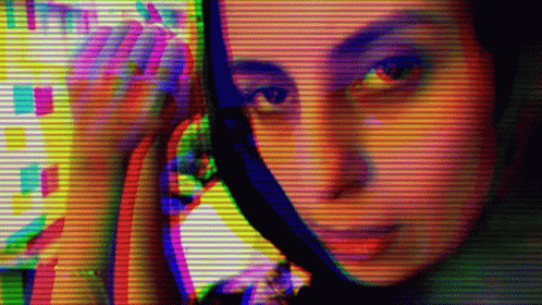 A Woman Looking At Herself In A Mirror With A Rainbow Colored Background GIF