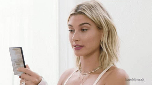 A Woman Looking At Herself In A Mirror With Bareminerals Written On The Bottom Right GIF