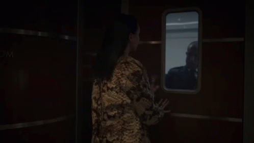 A Woman Looking Out A Window With A Sign That Says Wc GIF