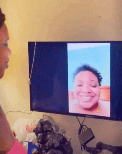 A Woman Looks At A Picture Of Herself On A Tv Screen GIF