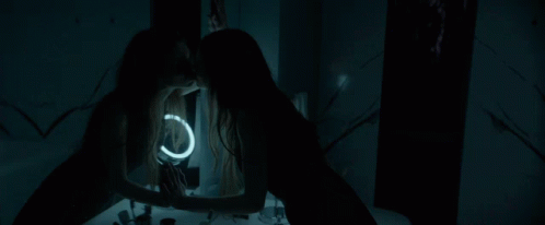 A Woman Looks At Her Reflection In A Mirror With A Light Ring GIF
