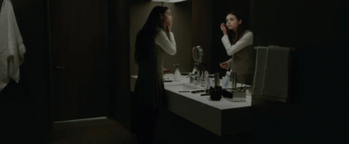 A Woman Looks At Herself In A Bathroom Mirror GIF