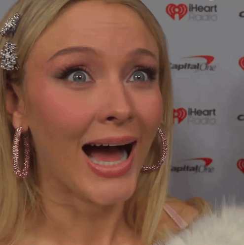 A Woman Making A Funny Face In Front Of A Capital One Heart Radio Sign GIF