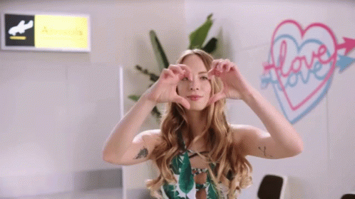 A Woman Making A Heart Shape With Her Hands In Front Of A Sign That Says Love GIF