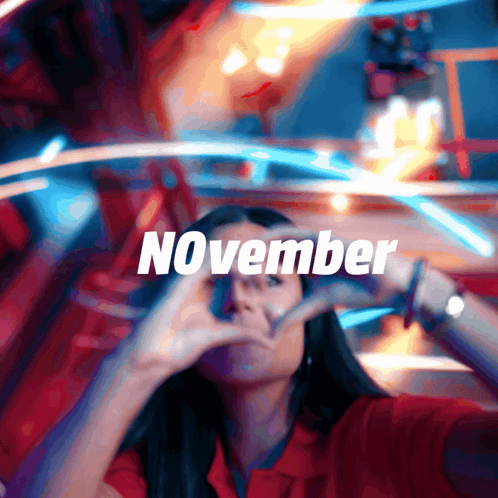 A Woman Making A Heart Shape With Her Hands In Front Of A Sign That Says November GIF