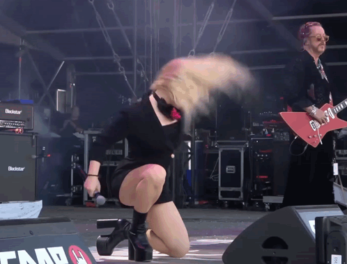 A Woman On Stage With A Microphone In Front Of A Blackstar Guitar Amplifier GIF