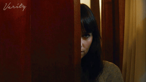 A Woman Peeking Out From Behind A Door With The Word Verity Written On It GIF