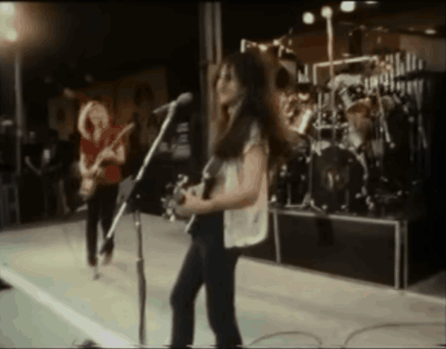 A Woman Playing A Guitar And Singing Into A Microphone On Stage GIF