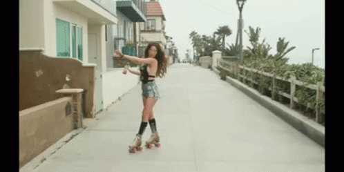 A Woman Rollerblading Down A Sidewalk Holding A Bottle GIF