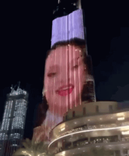A Woman 'S Face Is Projected On A Building At Night GIF