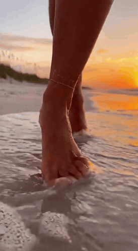 A Woman 'S Feet Are Walking On The Beach At Sunset . GIF