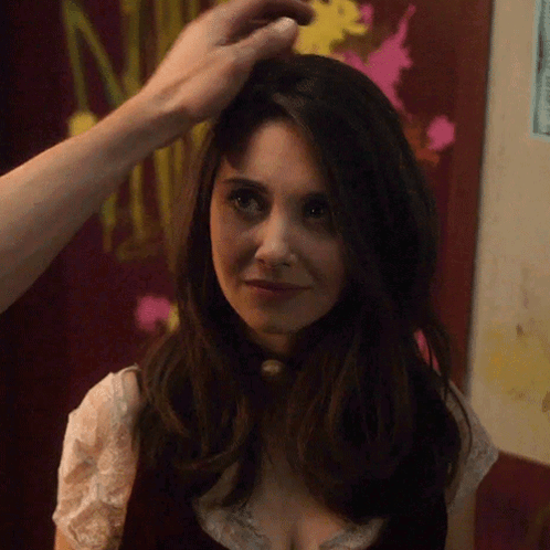 A Woman 'S Hair Is Being Touched By A Man In Front Of A Sign That Says N. GIF