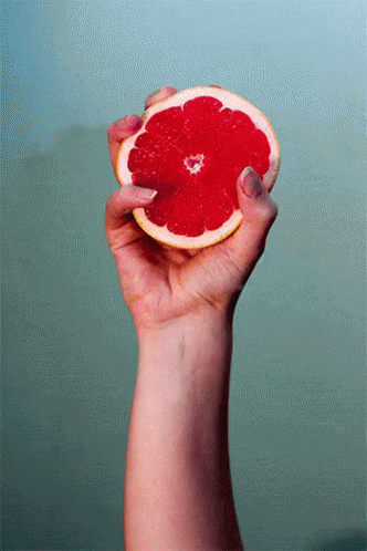 A Woman 'S Hand Is Holding A Slice Of Grapefruit In Her Right Hand GIF