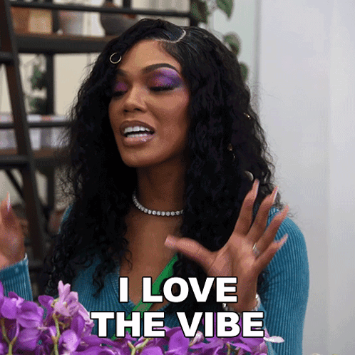 A Woman Says I Love The Vibe In Front Of Some Purple Flowers GIF