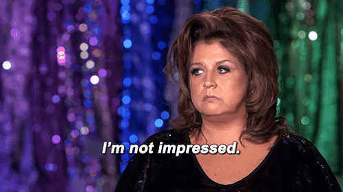 A Woman Says " I 'M Not Impressed " In Front Of Purple And Green Curtain GIF