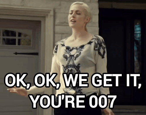 A Woman Says Ok Ok We Get It You 'Re 007 While Standing In Front Of A Garage Door GIF