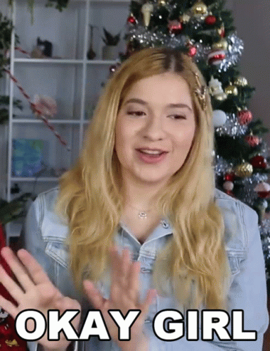 A Woman Says Okay Girl With A Christmas Tree In The Background GIF