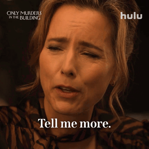 A Woman Says " Tell Me More " In Front Of A Poster For Only Murders In The Building GIF