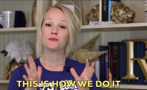 a woman says " this is how we do it " in front of a bookshelf