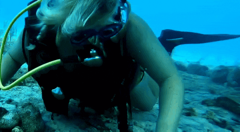 A Woman Scuba Diving In The Ocean With A Yellow Hose Coming Out Of Her Mouth GIF