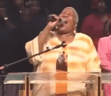A Woman Singing Into A Microphone At A Podium GIF