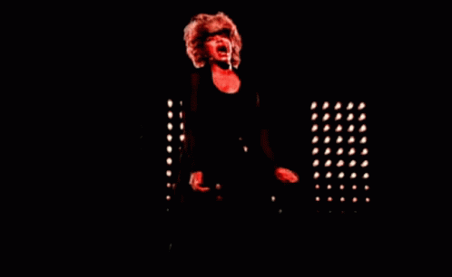 A Woman Singing Into A Microphone In A Dark Room With Red Lights GIF